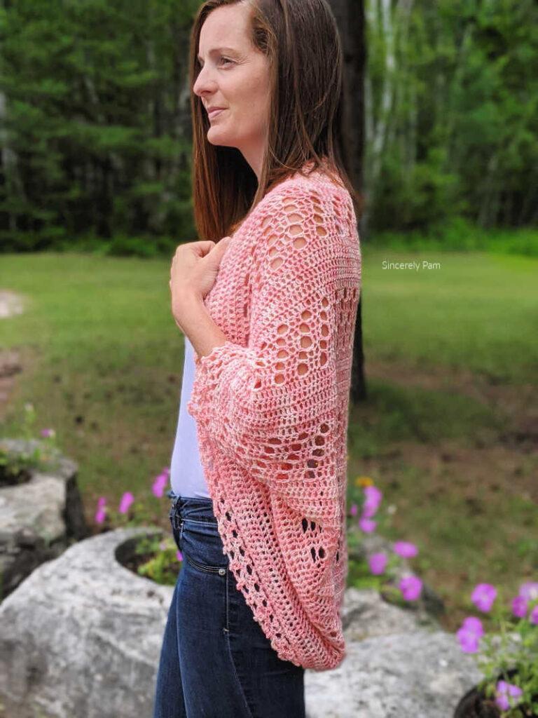 Model is standing in a garden while wearing the Daphne cocoon cardigan crochet pattern by Sincerely Pam