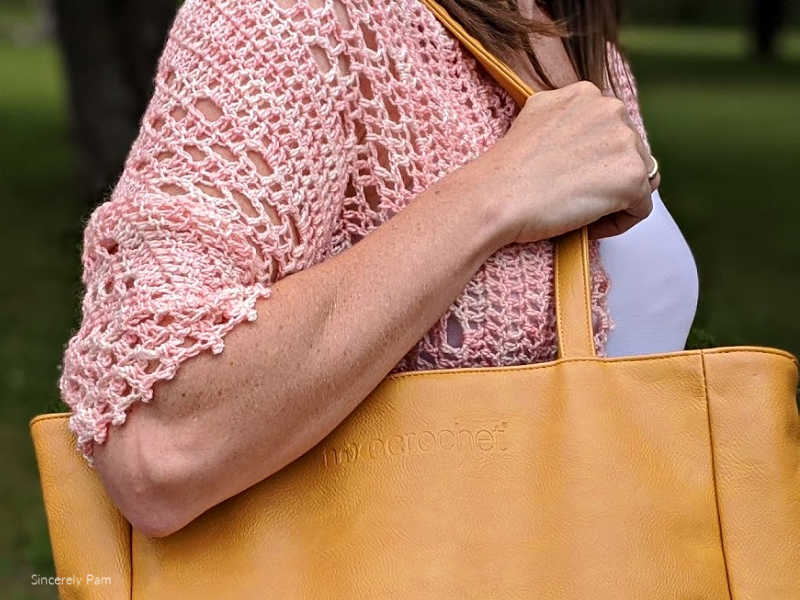 Model is wearing the Daphne cocoon cardigan crochet pattern by Sincerely Pam while holidng a saffron wecrochet tote bag.