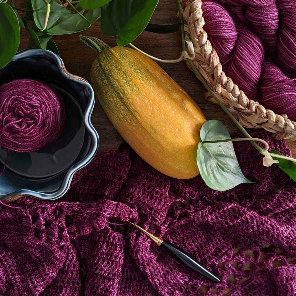 Contessa Cropped Pullover crochet pattern is being worked on a table top. Also shown is a squash and furls odyssey hook.