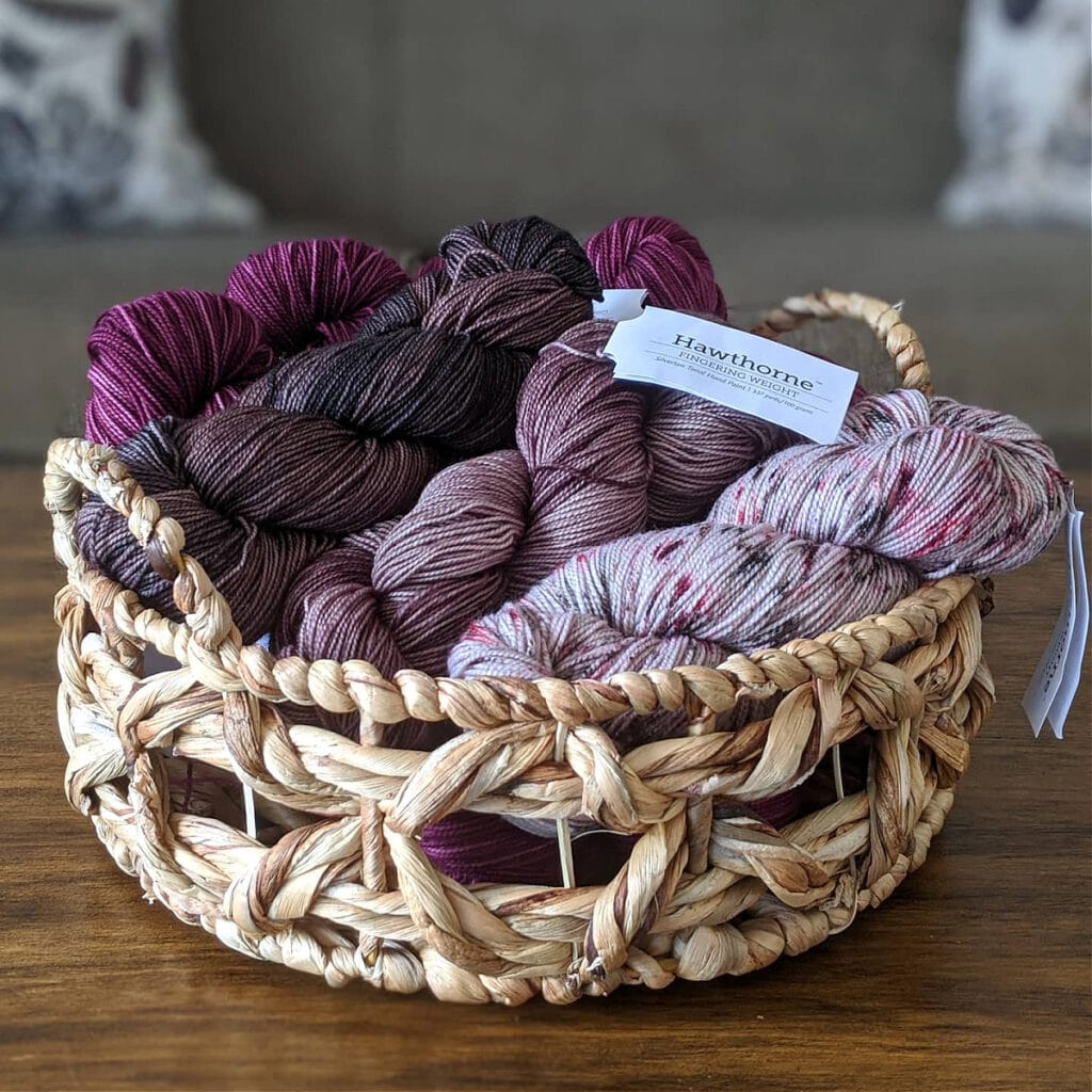 A basket filled with Hawthorne Fingering yarn by WeCrochet sits on a wooden table.