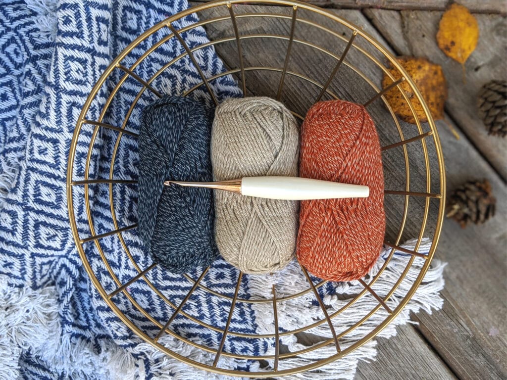 Kindred yarn from wecrochet sits in a brass bowl on a blue and white blanket. A Furls odyssey crochet hook sits on top.