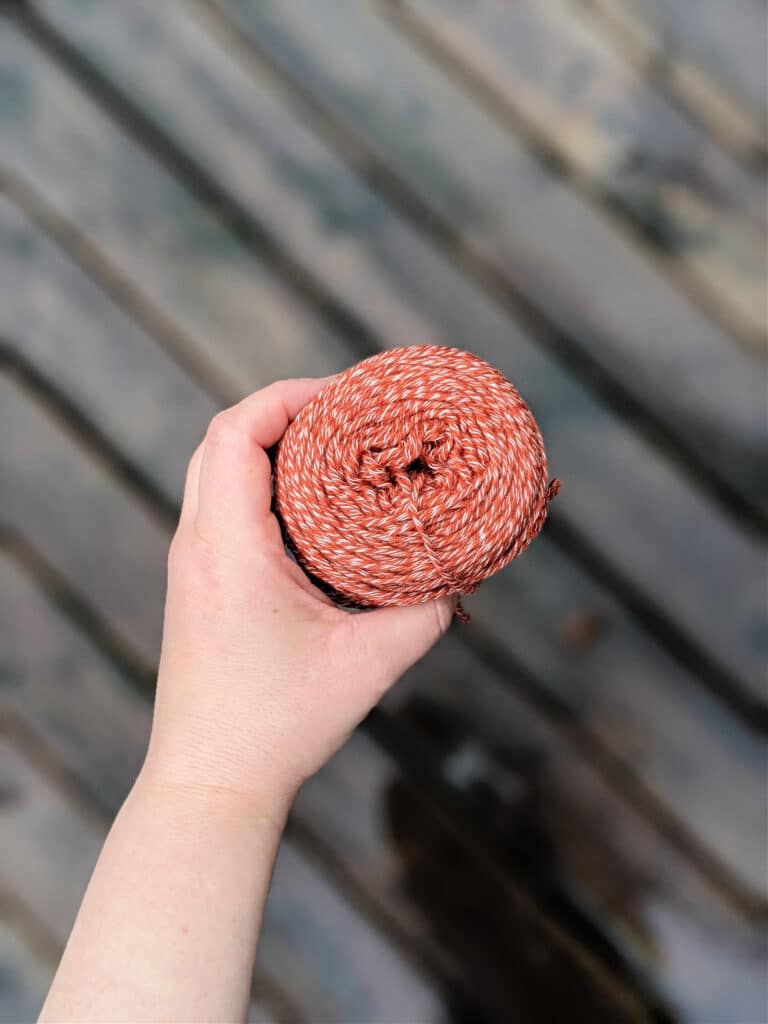 A hand holds a cake of Kindred yarn in color Spice over a wooden background.