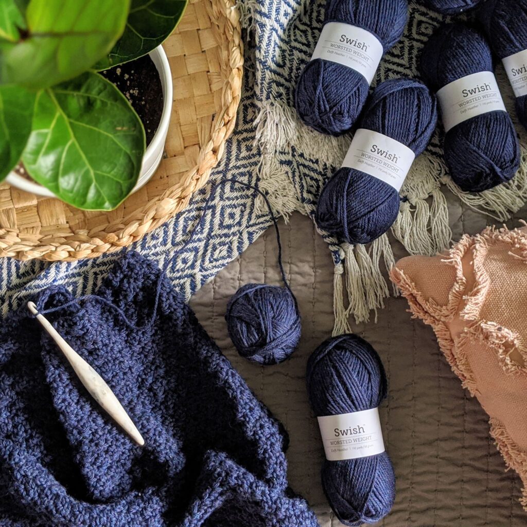 Swish worsted yarn from wecrochet is strewn on a bed.