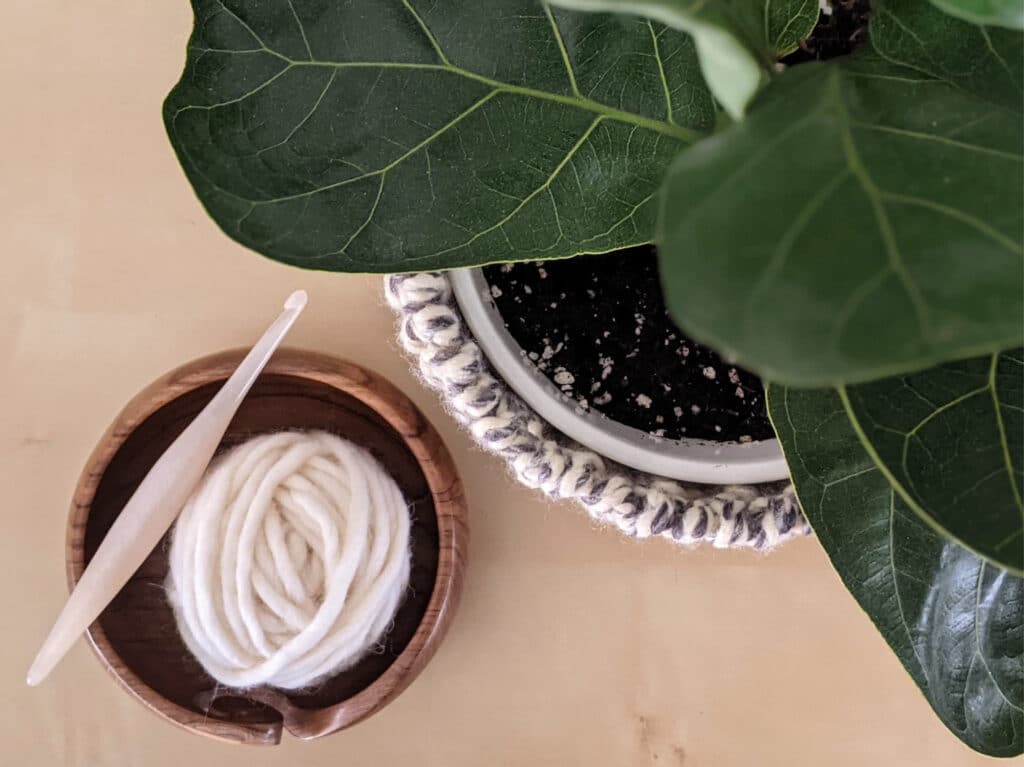 Overhead shot of the basket covering a plant pot. A ball of yarn and hook sits beside it.