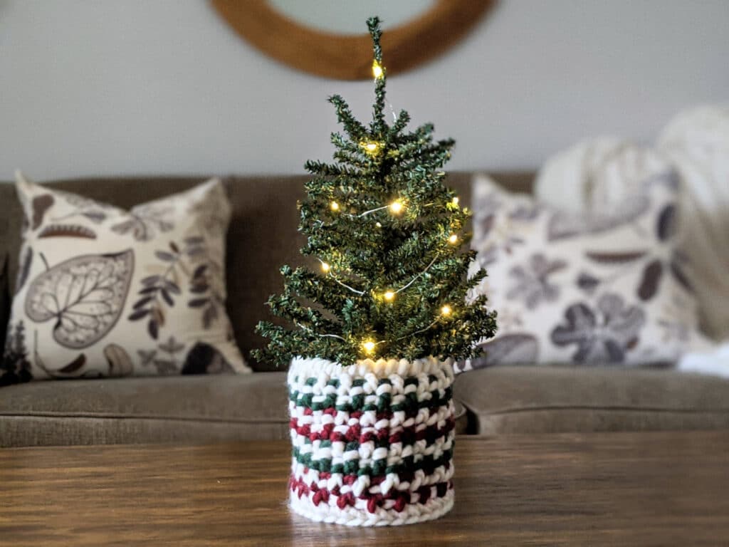 A totally textured crochet basket in Tuff Puff yarn sits on a table holding a mini Christmas tree.