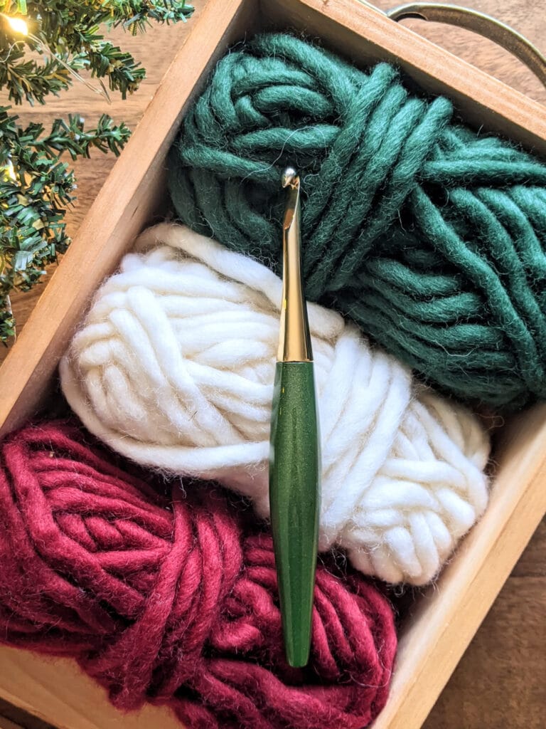 A green Odyssey Furls crochet hook sits on top of a couple balls of WeCrochet Tuff Puff yarn.